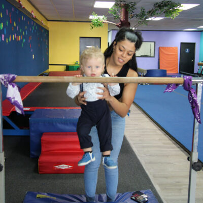 a woman holding a little boy up to a parallel bar.