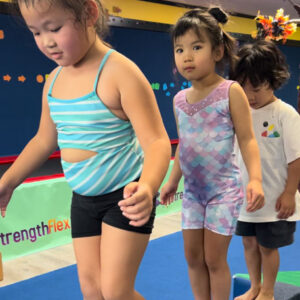 Three young children walking across a gymnastics' beam.
