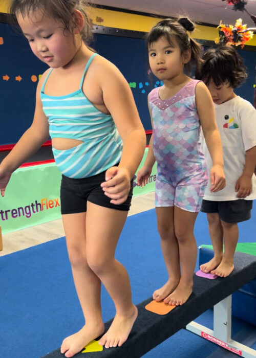 Three young children walking across a gymnastics' beam.