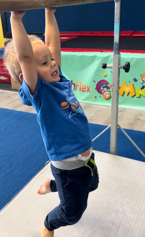 Cute toddler boy hanging from gymnastics' bar.
